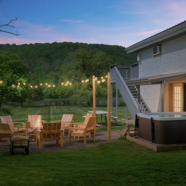 The Hog Mountain Chalet backyard at dusk with hot tub, fire pit seating and mountain views in Fleischmanns, NY